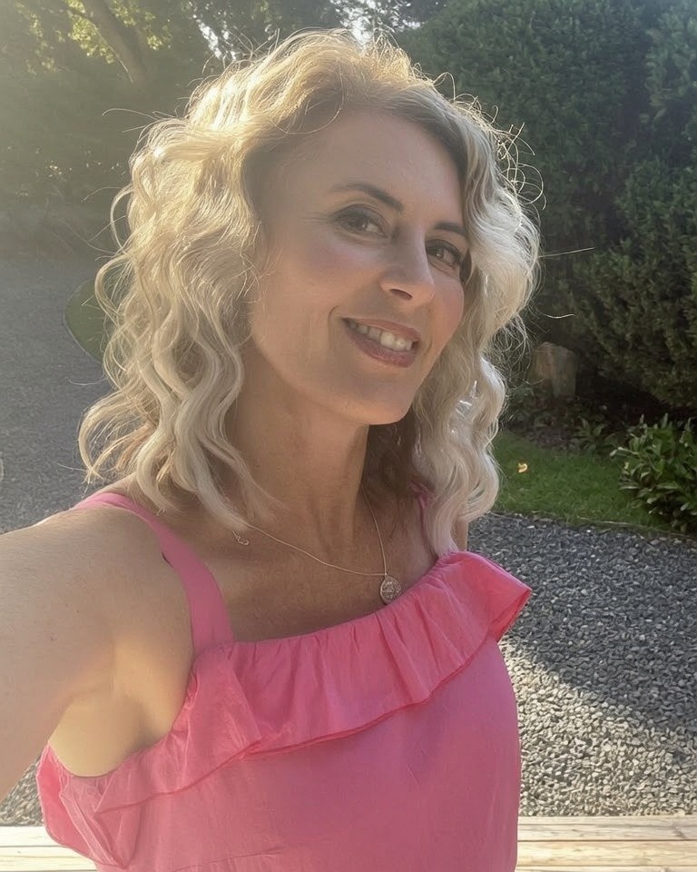 Kate, smiling, outdoors in a sunlit garden
